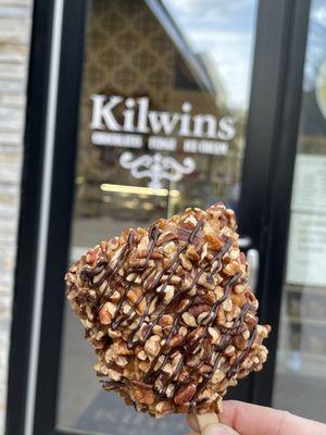 Rice crispy treat covered in nuts drizzled in dark chocolate.