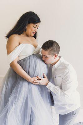 a father kisses his wife's pregnant belly in a maternity photo shoot in a studio