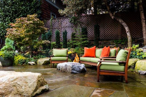 Flagstone compliments verdant woodland plantings. A natural gas, easy-care fire feature is set in a custom hewn granite boulder.