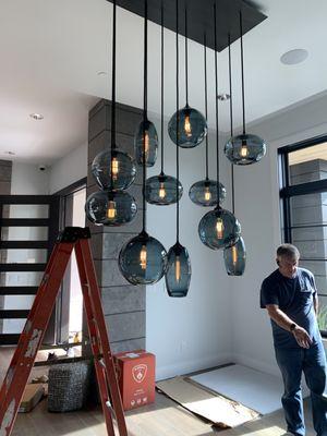 Installing custom designer glass & metal chandelier light for dinning room fixture.