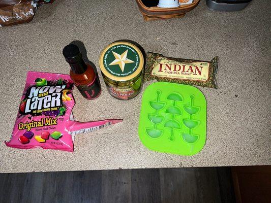 now and later candies, spicy okra pickles, hot sauce, vegan indian samosa wrap and an ice cube tray.