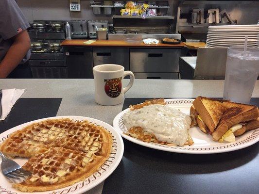 Waffles, coffee, hash browns covered in gravy, and an egg sandwich