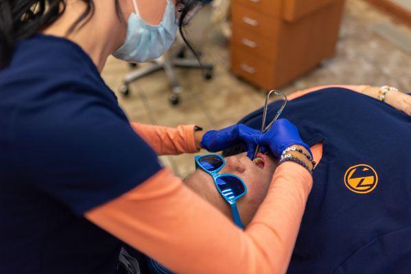 An orthodontic clinical assistant performs a braces adjustment on a team member in treatment.