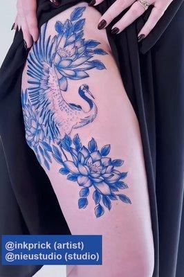 Tattoo on the right thigh, all blue and resembling porcelain, featuring a lotus flower on top and bottom with a crane in flight between.