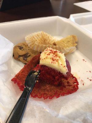 Red velvet cupcake. With one of their chocolate chip cookies hiding in the background