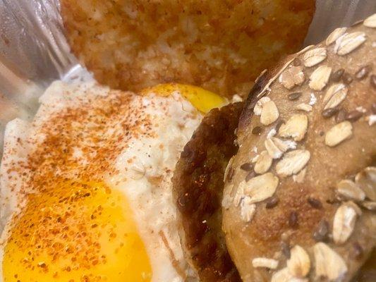 Sunny side up eggs Hasbrown patty sausage patty and oat/flax bagel