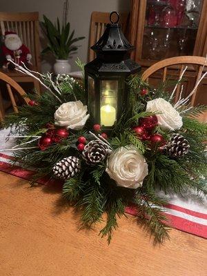 Lantern centerpiece with Flameless candle, seasonal greens, white roses, hypericum, pinecones, glass balls with twigs.