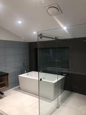 Glass tile wall with freestanding tub and frameless/curb-less shower