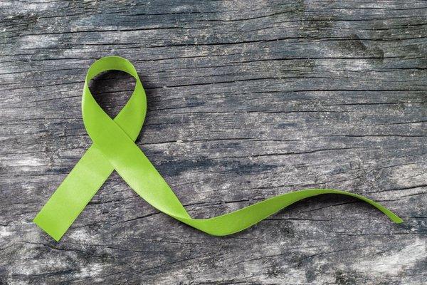 green awareness ribbon on faded grey wood