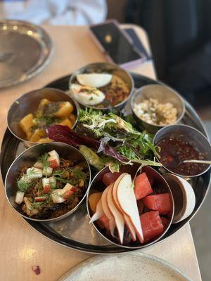 Tusk Breakfast featuring: hummus, hard boiled egg, dates, fresh fruit, green salad, popped grains, red zhoug