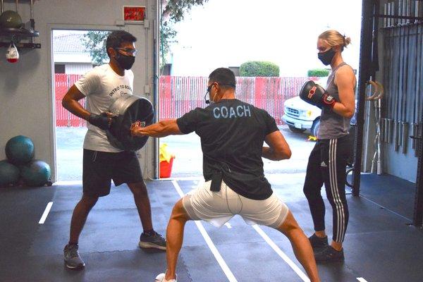 Coach cueing participants of our 4 Week Boxing Program as they work in pairs practicing to hold and punch the shield.