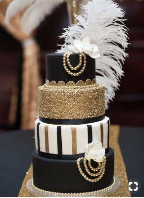 4 tiered quinceañera cake adorned with white feathers and gold pearls. a glittery middle tier and white flowers.