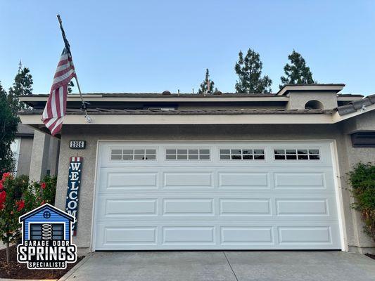 Recently installed white long-panel double car garage door with windows, adding modern style and increased natural light.