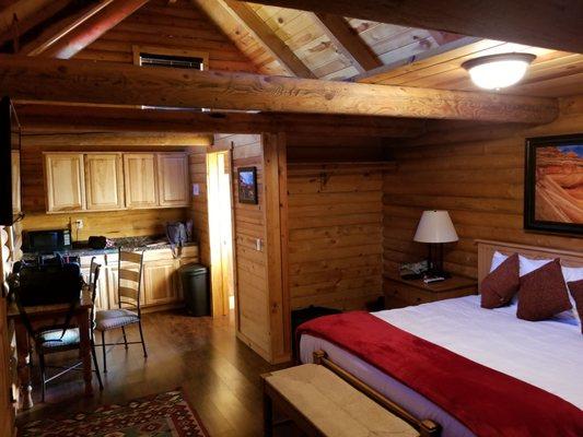 View of the bed and "kitchen" area that has a mini fridge, a microwave oven, and a table.