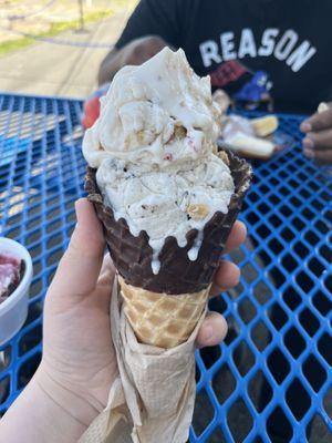 Strawberry cheesecake scoop and a cookies and cream scoop in a chocolate dipped waffle cone.