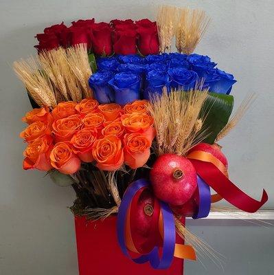 Beautiful red box arrangement with red, blue, and orange roses, wheat straw, pomegranate, and greenery.