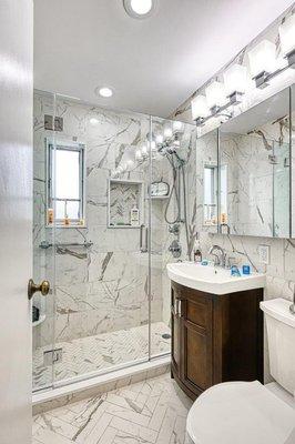 Exquisite:  Statuario marbelized porcelain tile:  12x24 walls, 3x12 bathroom floor, 12x12 shower floor & niche:  mosaic herringbone.