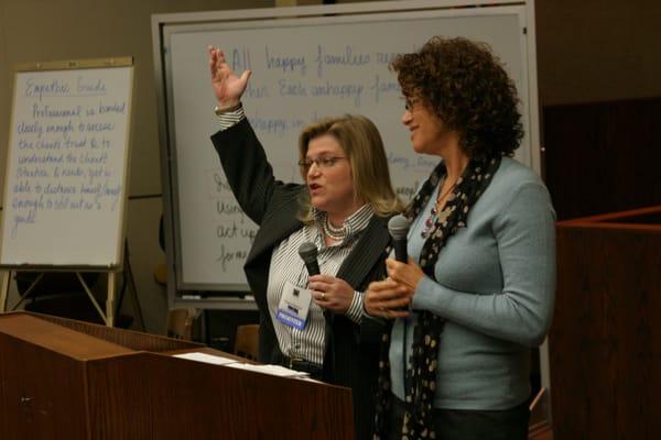 Diana Mercer (background) presents at a conference. In addition to our mediation services, our mediators teach and train.