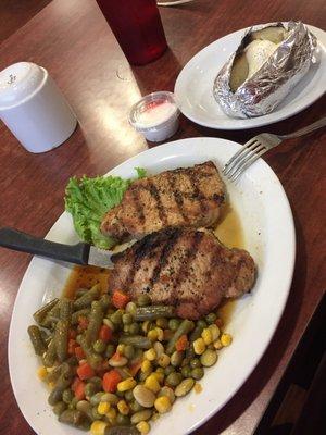 Grilled pork chops with a baked potato and mixed vegetables.