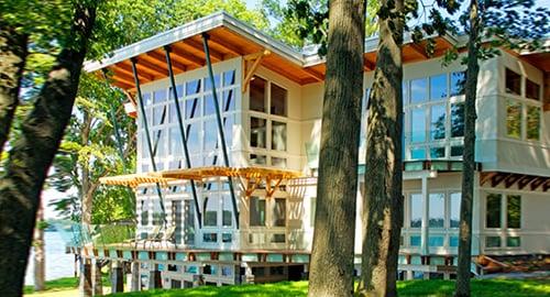 Modern home with glass railing deck around a full window wall view facing lake.