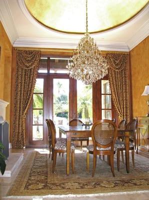 Dining room drapes with swags in this Rancho Santa Fe home draw the eye up to its gold leafed, domed ceiling.