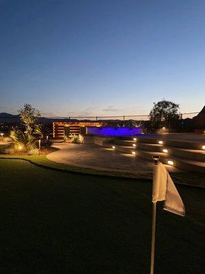 Upclose putting green with perfectly lit backdrop of spa, pots and natural wood equipment wall