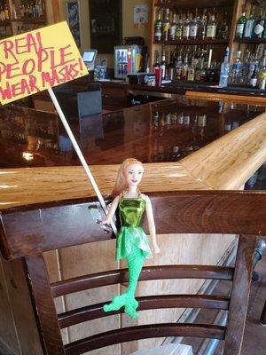 A barbie doll in a chair to let patrons know they cannot sit at the bar due to covid, lol