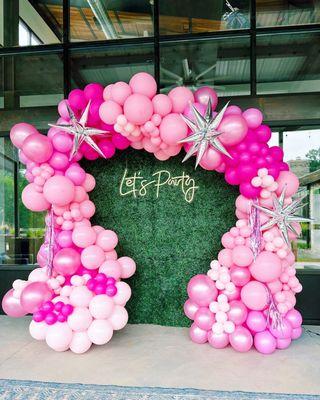 Neon sign on greenery backdrop with balloon garland arching over the backdrop.