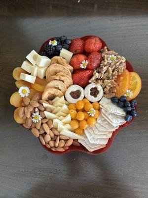 A vegetarian charcuterie board with almonds, cheese, crackers, fruit, and flowers.