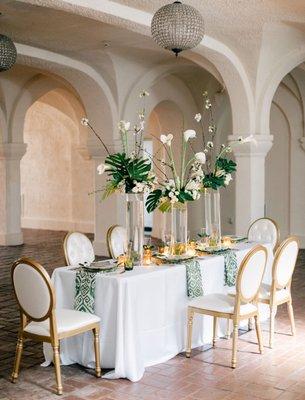 Stunning floral table scape of calla lilies, large graphic leaves and orchids, fit for a king & queen and their guest.