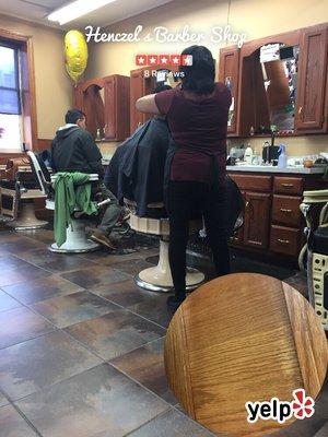 Getting a hair and beard trimmed.  The lady who is tending to him seems to know what she is doing .