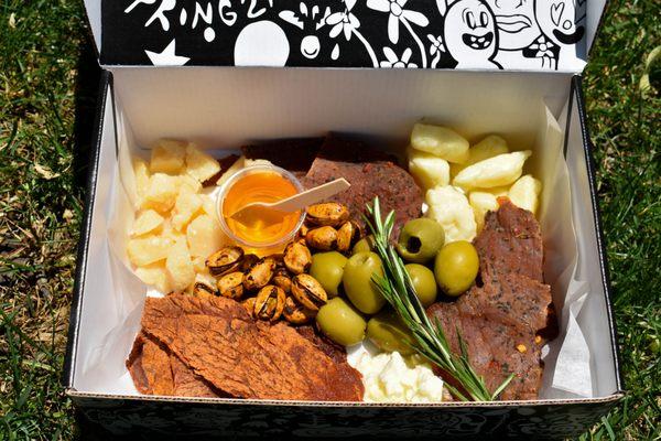 "Please Smile" Artist Box: Beef Jerky, Chili Basil Turkey Jerky, Cheddar Cheese Curds, Feta, Parmesan, Smokey Pistachios, Olives, Honey