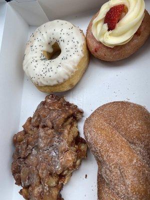 Partially eaten Apple Fritter, cinnamon sugar twist, lemon poppyseed donut and strawberry donut.