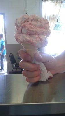 A satisfied customer with a Hershey's hand scooped strawberry cheesecake ice cream cone.