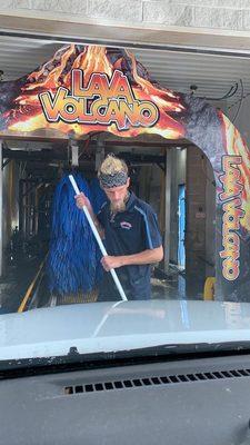 Car wash tunnel and employee scrubbing truck front end.