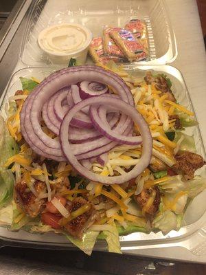 Grilled chicken salad with ranch dressing, it includes lettuce, tomato, cucumbers, cheese, marinated chicken topped off with onion