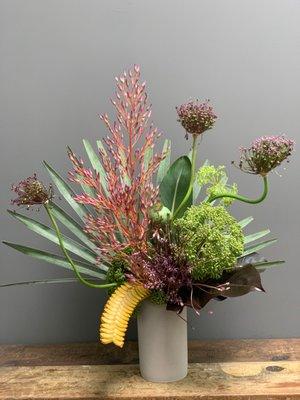 Bismarkia palm, bromeliads, alliums, strelitzia leaf, giant fennel, and rattlesnake plant in concrete vessel.