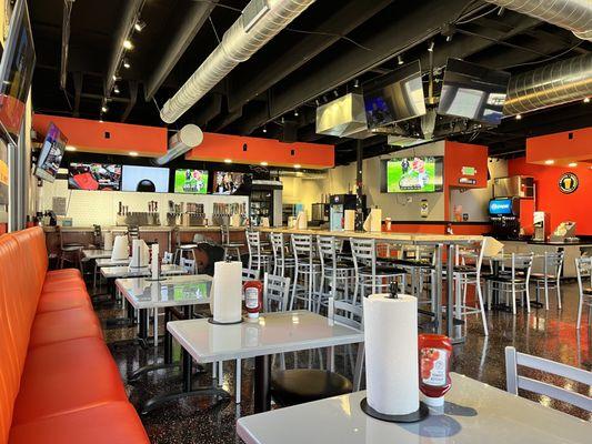 Inside dining area with bar stools, large table sections, and several TV's