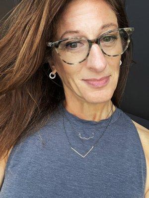 Woman in blue shirt, glasses and reddish shoulder length hair wearing two mixed metal necklaces purchased at Foamy Wader in Langley, WA.