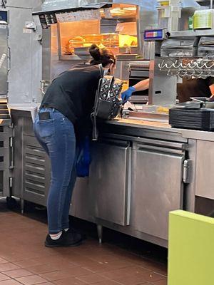 Worker standing over the food area on her phone with her backpack she placed on area where food was being made!