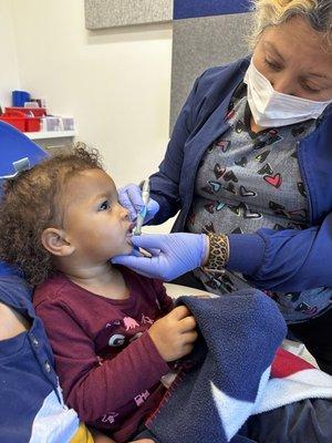 Baby girl watching tv next to big brother and having her teeth cleaned.