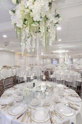 Crystal Chiavari Chairs with White Cushions, Ivory Linens, White Napkins, Gold Flatware, and Gold Beaded Chargers.