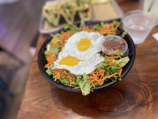 Gogi Bowl. It comes with carrots, green onions, mixed greens, two eggs (sunnyside up). The vegetables rest on top of a bed or white rice.