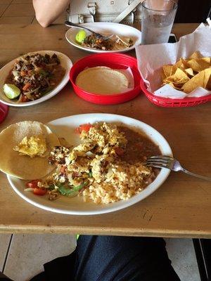 Scrambled eggs w/ bacon, beans, rice and tortillas, carne asada super taco to the left, small carnitas tacos in the middle.