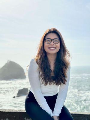 Jelissa "Jojo" Rempojo sits smiing with the ocean in the background.