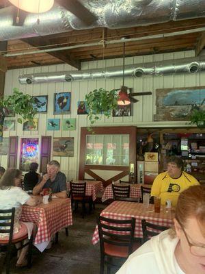 Inside the restaurant with several plants and paintings and even a guy wearing a pacer shirt.