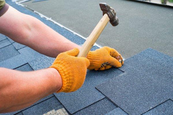 Worker Hands installing bitumen roof shingles using Hammer in nail