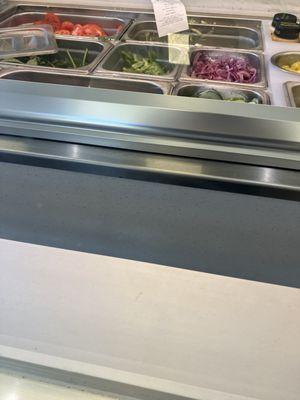 A dirty receipt hanging in the lettuce tray. White substance inside the cucumber tray and the onions are not fresh