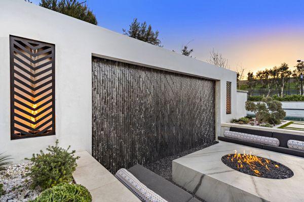 Weeping Waterwall framed with our signature fire cages behind a sunken fire pit with generous seating for 12 people