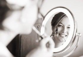 Beautiful bride looking into mirror while putting on makeup for her big day.